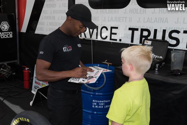 Antron Brown waved a fan into his pit area to give him and autograph while he prepared his fuel for his car.