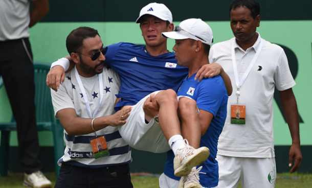 Korea's Seong Chan Hong being carried off the court after conceding in his singles rubber against Ramanathan (Photo by Money Sharma/AFP/Getty Images)