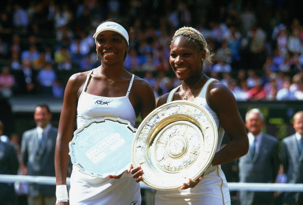 Serena Williams (R) poses with her sister Venus Williams (L) after winning her first Wimbledon title in 2002. (Photo by Mike Hewitt/Getty Images)