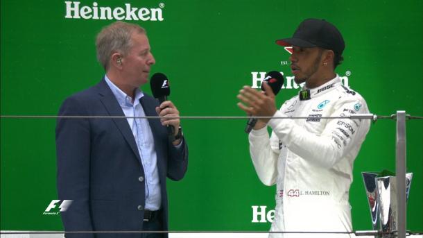 Ao lado de Martin Brundle, Lewis Hamilton fala no pódio sobre mais uma vitória (Foto: Divulgação/F1)