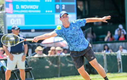 Dennis Novikov hits a forehand return to John Isner