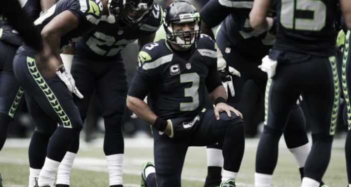 Seattle Seahawks quarterback Russell Wilson kneels in the huddle to read out a play to the offense in a game. Image via AP.