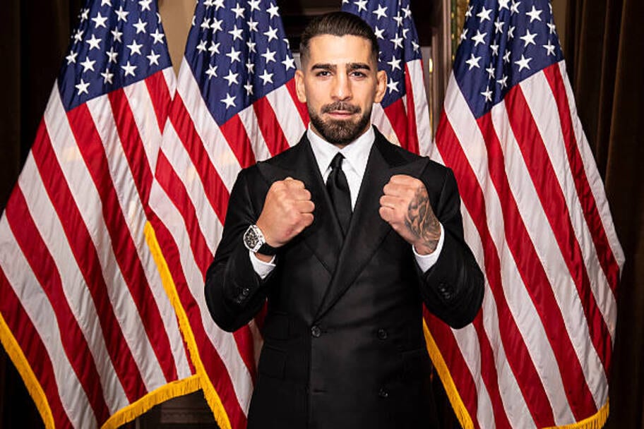 Ilia Topuria posing in a black suit before American flags in September 2026